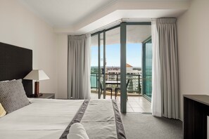 Ein Hotelzimmer mit Bett, Nachttisch, Lampe, einem Balkon mit Tisch und Stühlen sowie Blick auf die Stadt.