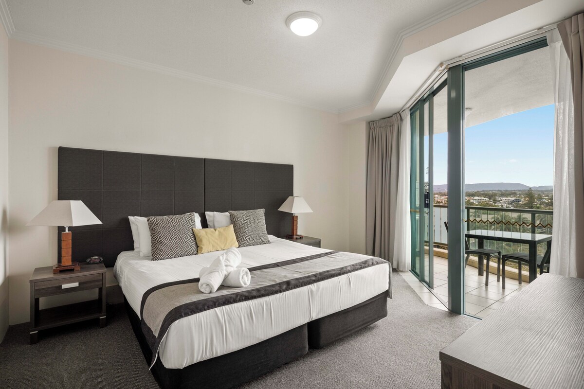 A hotel room with a large bed, two bedside tables, a desk, and a balcony with a view.