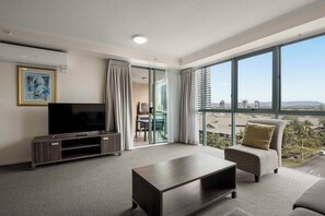 Ein modernes Wohnzimmer mit einem Flachbildfernseher, einem dunkelholznen Couchtisch, einem gemusterten Sessel und einem großen Fenster mit Blick auf die Stadt.