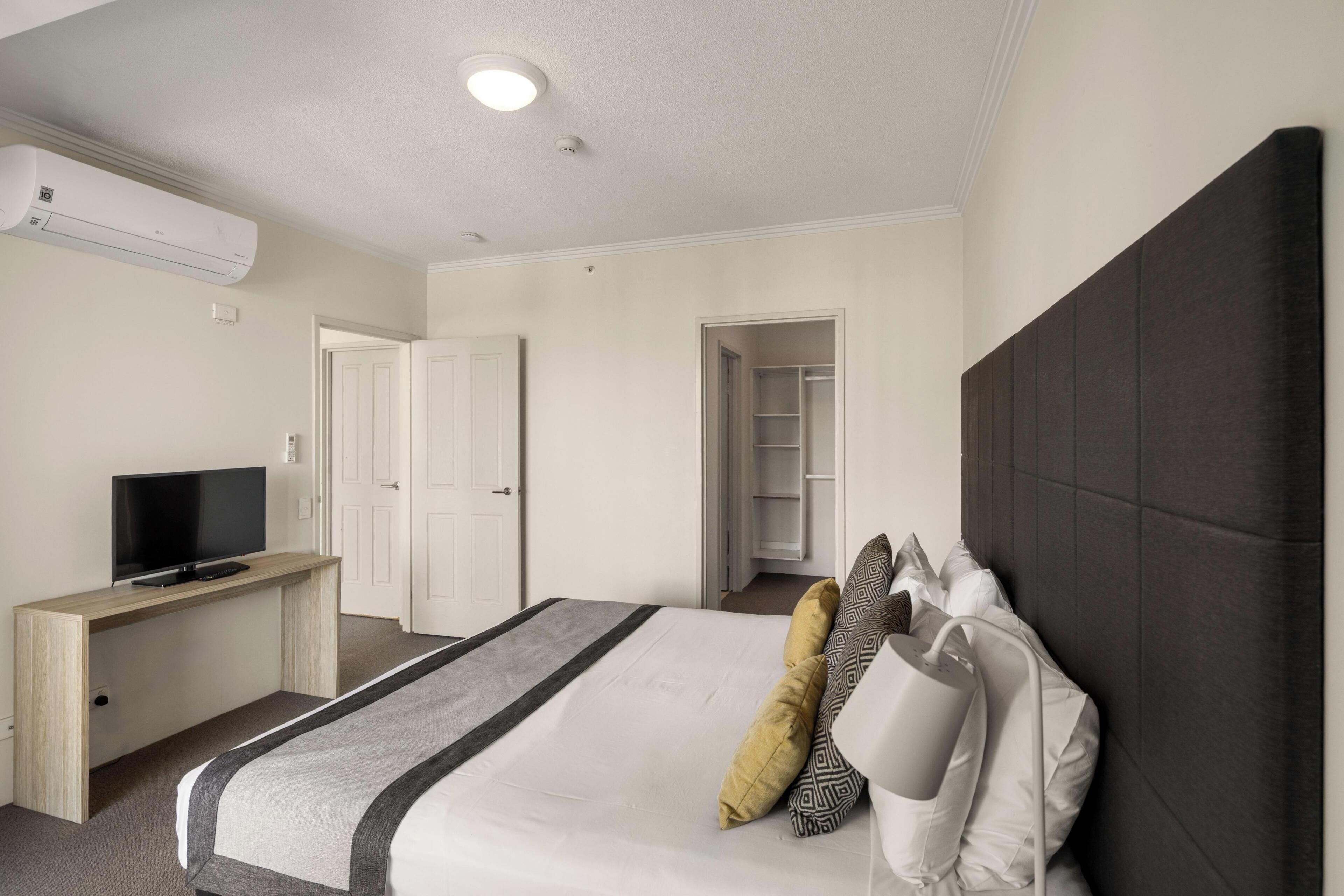 A hotel room with a bed, a desk with a TV, a wardrobe, and a closet.