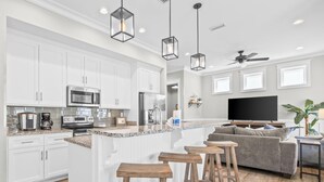 A modern kitchen with white cabinets, a central island with stools, a built-in microwave, and a large flat-screen TV. - Pelican Haven • Beach Access • Community Pool • Fishing Pier (Gulf Shores)