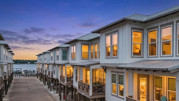 A waterfront row of white buildings with balconies, a wooden deck, and a view of the water. - Pelican Haven • Beach Access • Community Pool • Fishing Pier (Gulf Shores)