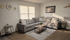 A living room with a grey sofa, a coffee table, a small side table, and a lamp. - Second Home Apartment, Close to Everything (Orangeburg)