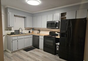 A modern kitchen with white cabinets, a black refrigerator, a microwave, and a stove.