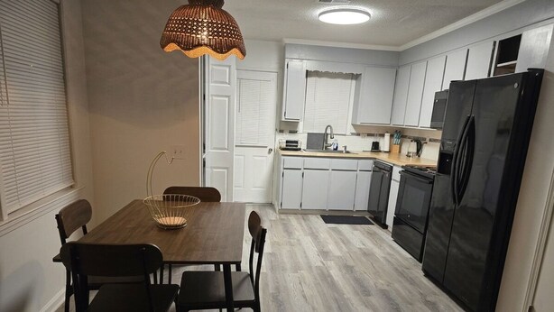 A modern kitchen with white cabinets, a black refrigerator, and a dining area with a wooden table and chairs. - Second Home Apartment, Close to Everything (Orangeburg)