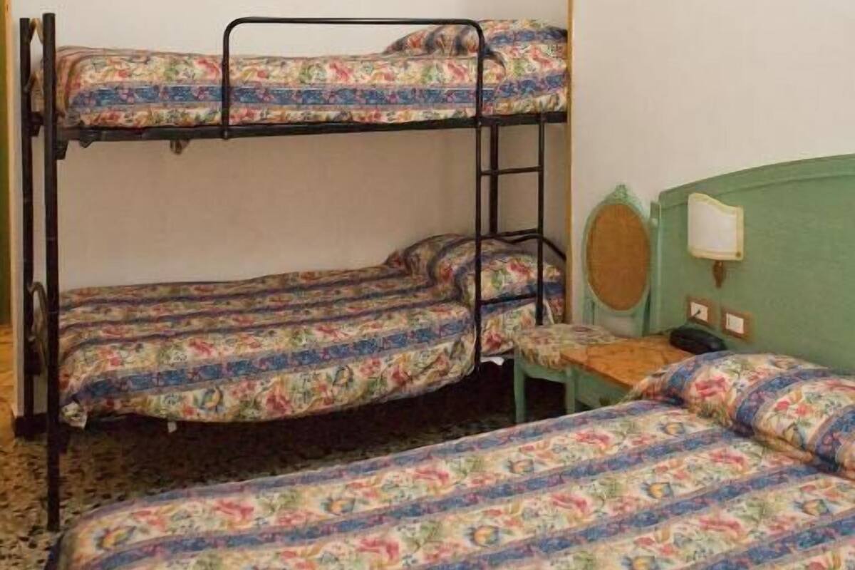 Une chambre avec des lits superposés, un ventilateur de plafond, une petite table et un mur vert.