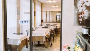 A restaurant with a glass door entrance, tables with white tablecloths, and a red leather bench. - hotel magnolia (Albenga)