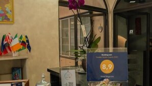 A hotel reception desk with a clock, flags, and a sign indicating a 8.9 rating. - hotel magnolia (Albenga)