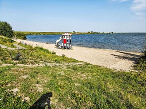 A beach with a small structure, a sandy path, and a body of water.