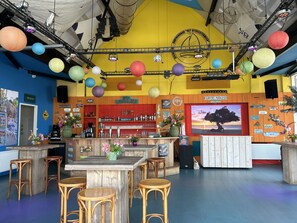 Een gezellig bar met houten meubels, een groot scherm waarop een strandafbeelding staat, en diverse borden en decoraties.