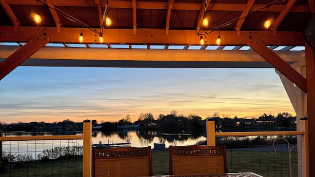 A covered outdoor seating area with a view of a lake and distant buildings. - Lakefront Escape Near Gorge Amphitheater (Moses Lake)