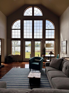 A spacious living room with large arched windows, a comfortable sofa, a small table, and a lamp. - Lakefront Escape Near Gorge Amphitheater (Moses Lake)