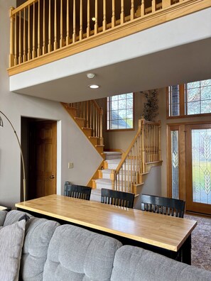 A dining area with a wooden table and chairs, a staircase with wooden railings, and a view of the outdoors through large windows. - Lakefront Escape Near Gorge Amphitheater (Moses Lake)