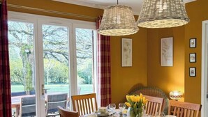 A dining area with a table set for four, two hanging wicker lamps, and a view through large glass doors to the outdoors. - Le Mûrier - GRAMAT - Gîte (GRAMAT)