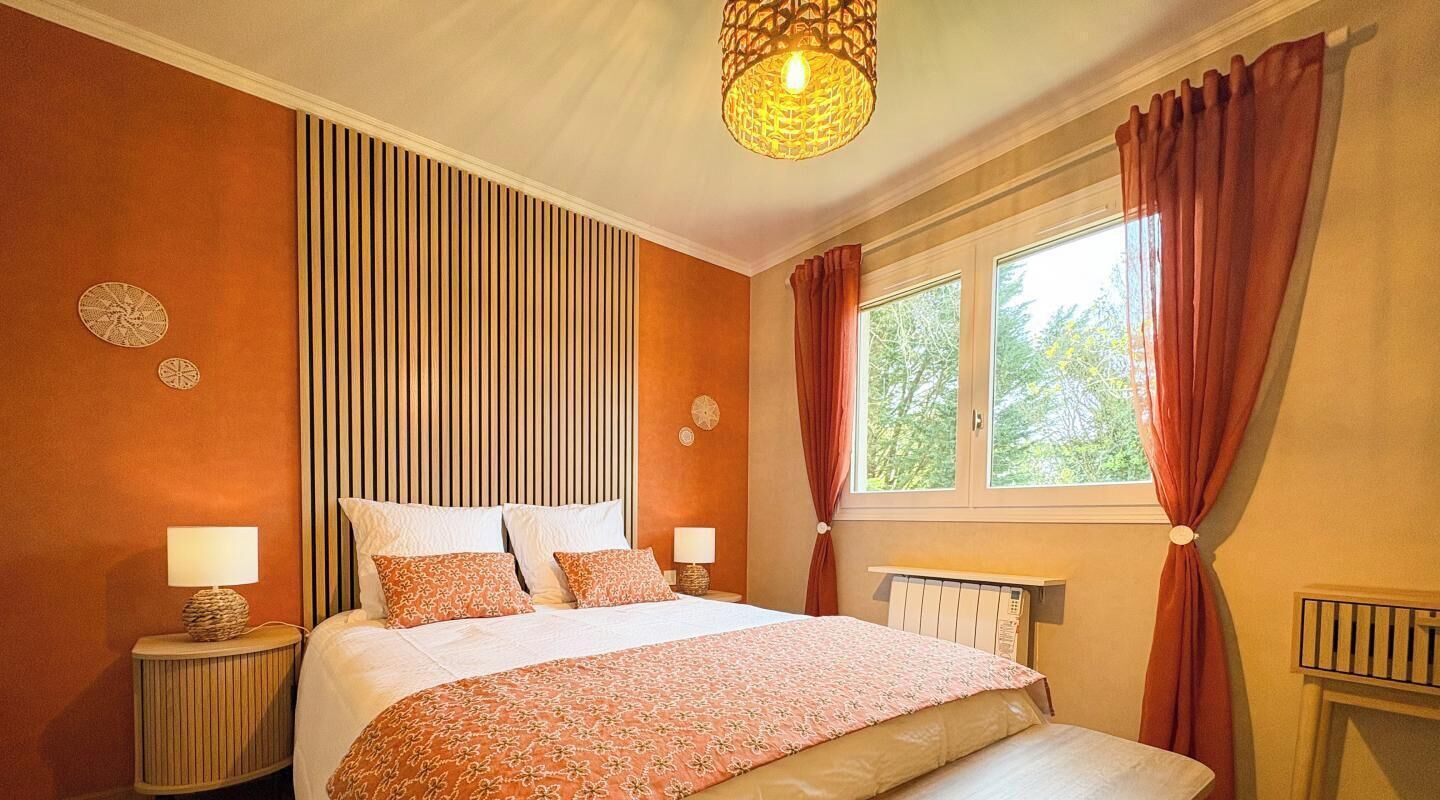 Een slaapkamer met een bed, een raam met gordijnen, een radiator en een wandlamp.
