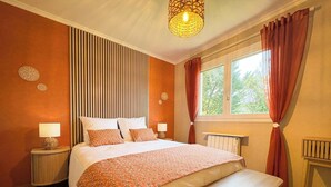 A bedroom with a bed, a window with curtains, a radiator, and a wall-mounted lamp. - Le Mûrier - GRAMAT - Gîte (GRAMAT)