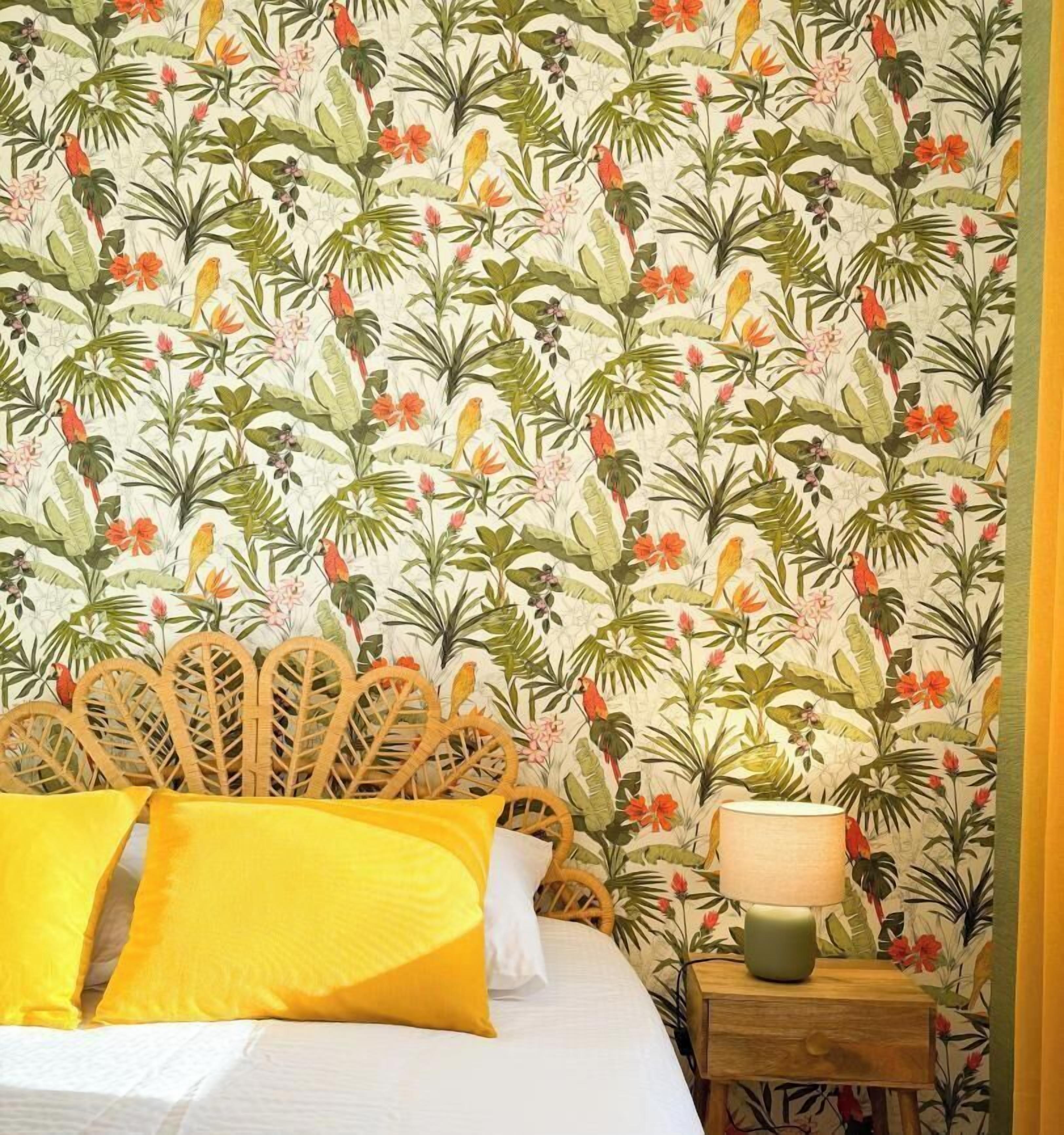 Een slaapkamer met een bed, een houten hoofdeinde, een nachtkastje met een lamp en tropisch behang.