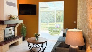 A living room with a fireplace, a sofa, a coffee table, and a TV mounted on the wall. - Le Mûrier - GRAMAT - Gîte (GRAMAT)