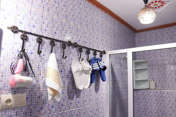 Un baño con pared de azulejos, zona de ducha y un perchero con distintos objetos.