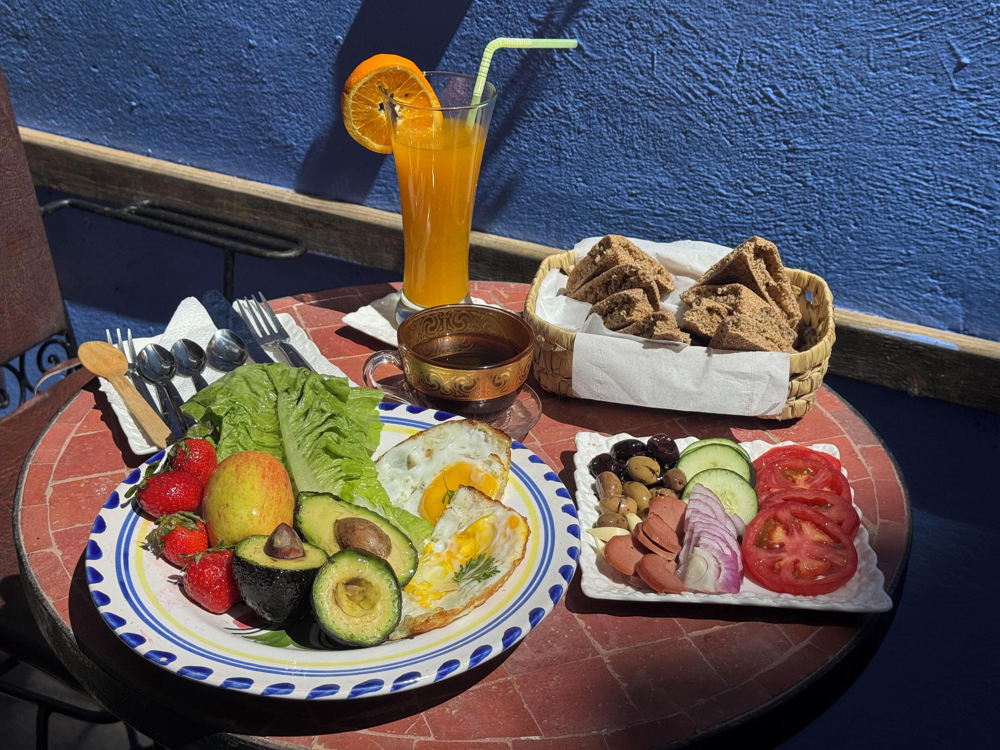 A breakfast table with a plate of fruits, vegetables, eggs, toast, and a drink.