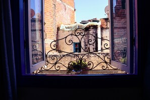 A window with a wrought iron balcony railing, a small door, and a view of a brick building.