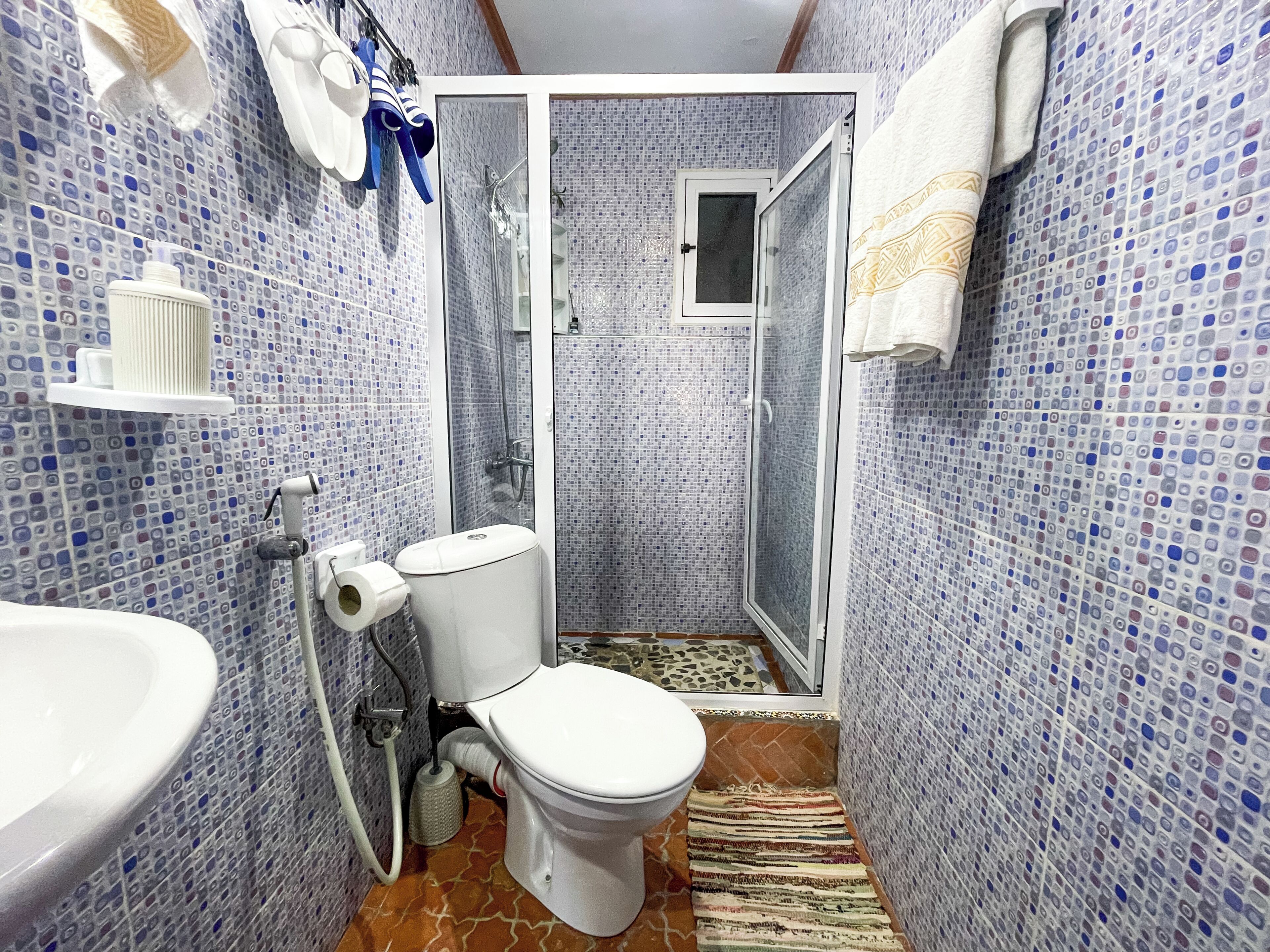 A bathroom with a toilet, sink, shower, and tiled walls.