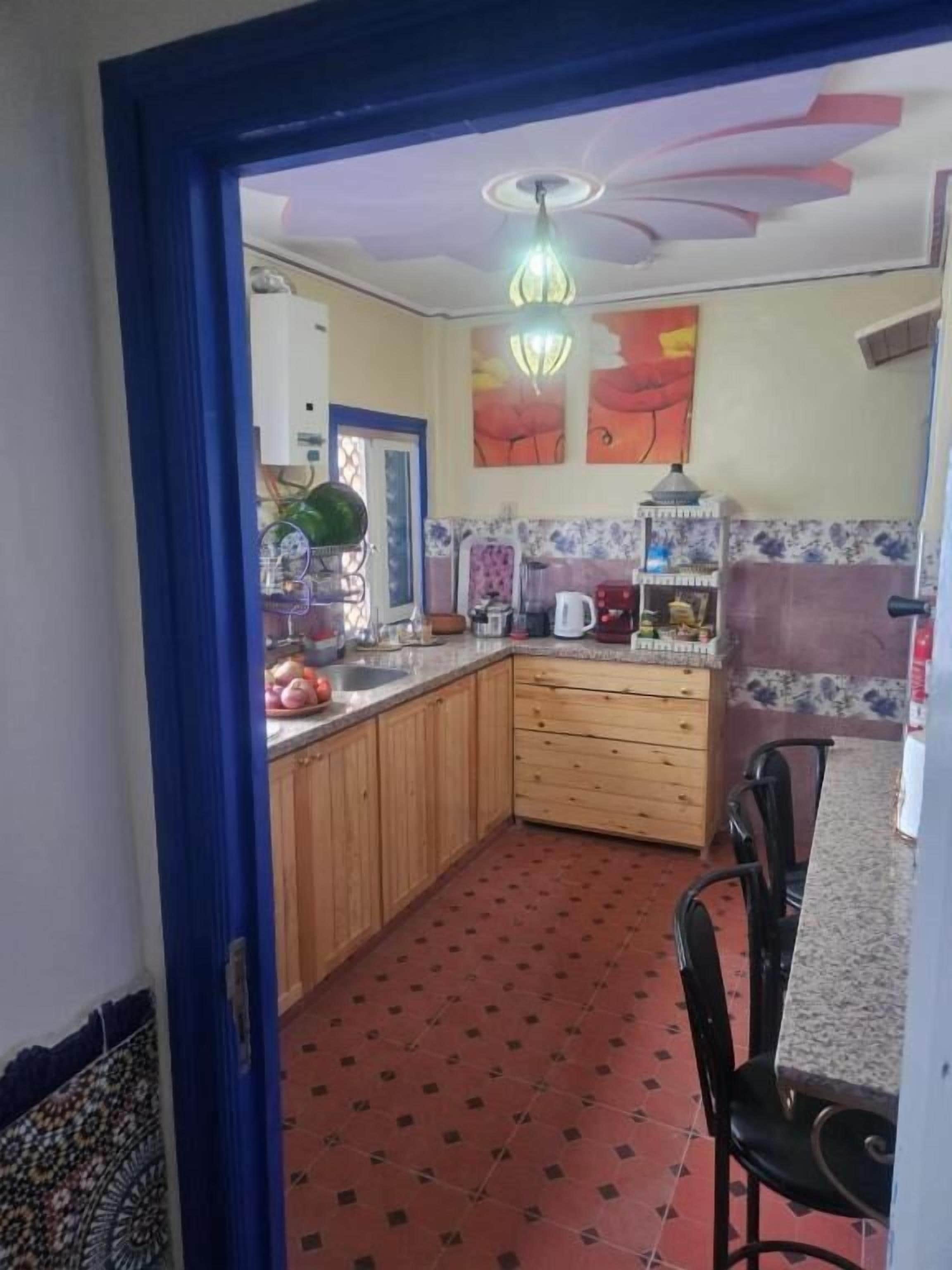 A kitchen with wooden cabinets, a tiled floor, and a dining area with chairs.