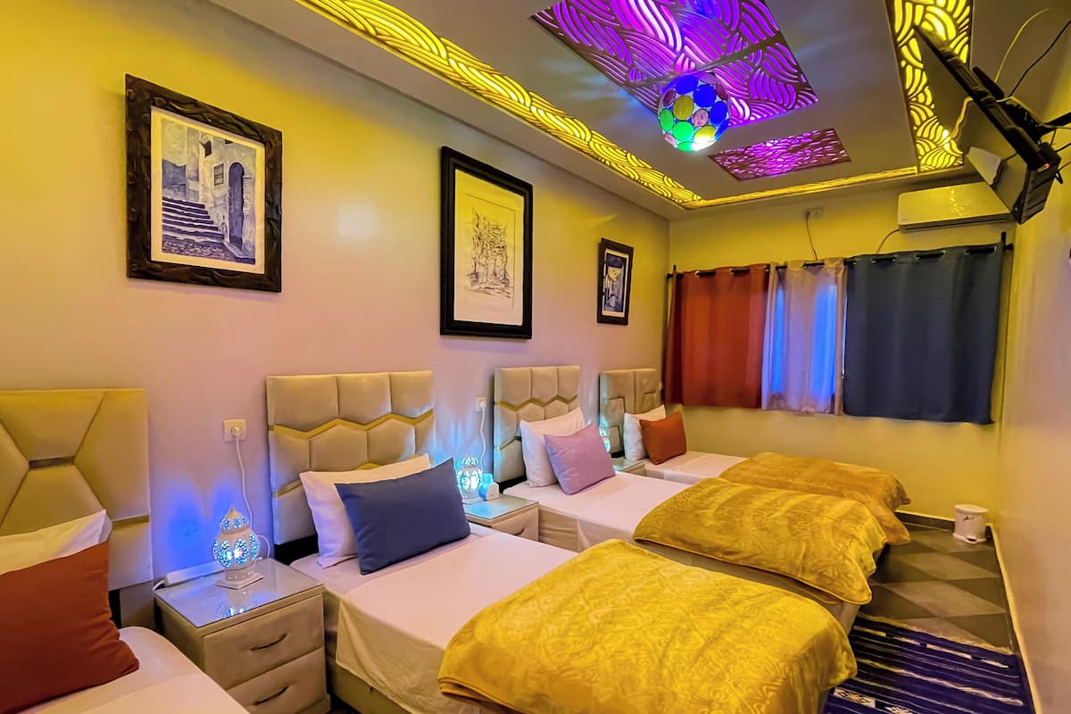 A hotel room with three beds, a ceiling light fixture, and framed artwork on the walls.