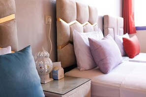 A neatly made bed with a headboard, a bedside table with a lamp, and a nightstand with a tissue box.