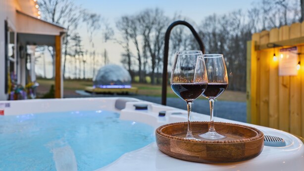 Un bain à remous avec deux verres de vin rouge posés sur un plateau en bois.