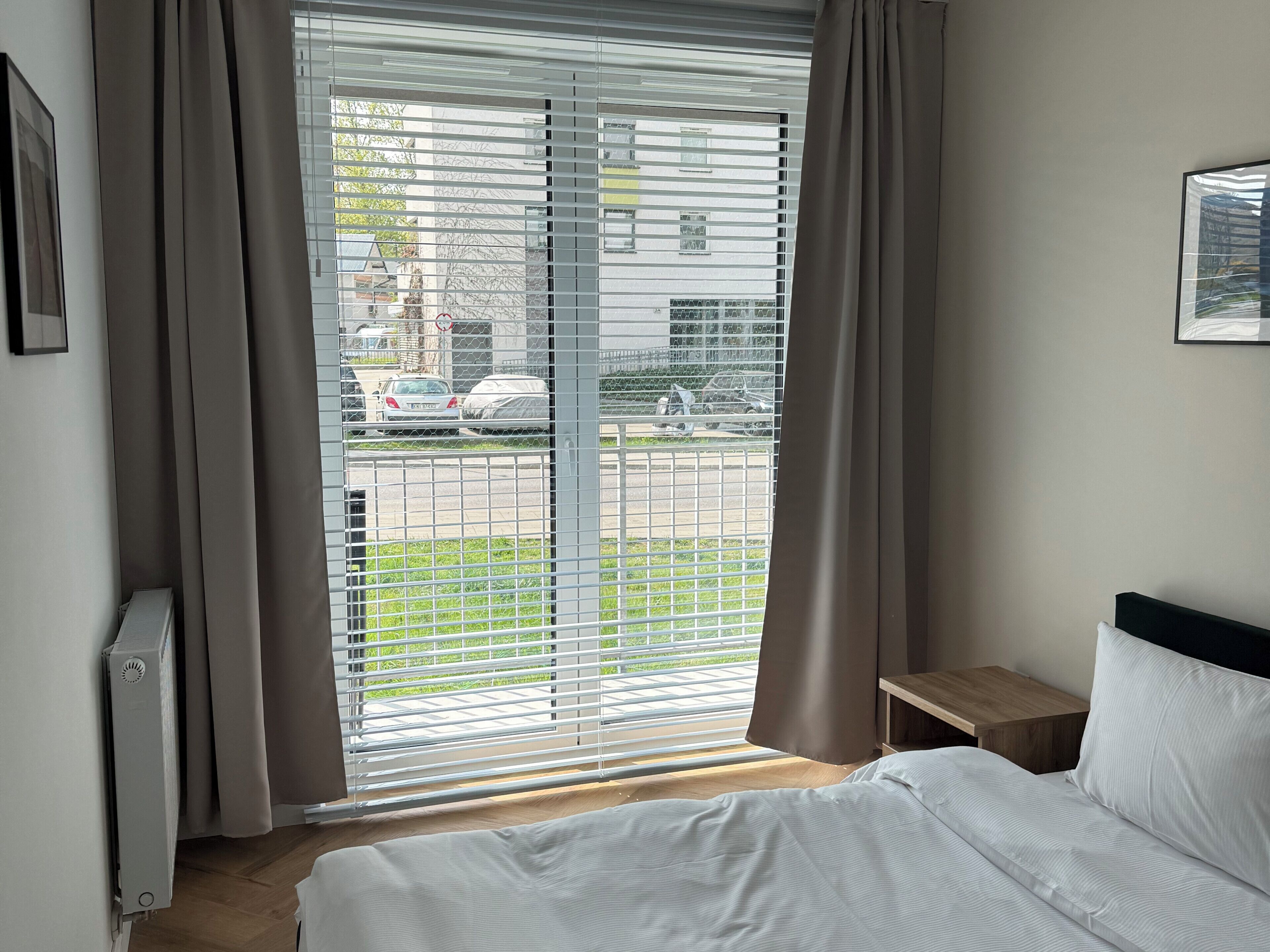 Een hotelkamer met een bed, nachtkastje, radiator en raam met jaloezieën.
