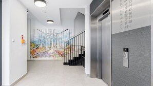 Un ascenseur moderne doté d’un écran numérique, un escalier avec une rampe en métal et une fresque colorée sur le mur.