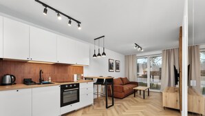 Une cuisine moderne avec un parquet en chevrons, un coin repas doté d’un canapé marron et une grande fenêtre agrémentée de rideaux.