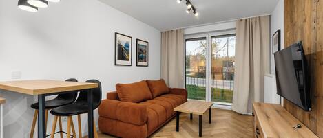 A modern living room with a sofa, dining table, chairs, a TV, and a large window.