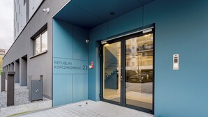 Une entrée d’immeuble avec une façade bleue, une porte en verre et un panneau indiquant la sortie de secours.