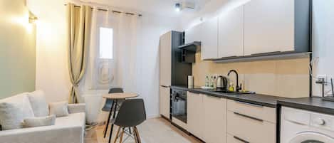 A compact kitchen with a dining area, a washing machine, and a window with curtains.