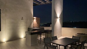 Patio esterno con barbecue, zona salotto e vista sulla città di notte.