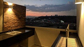 Un balcone con vista sulla città al crepuscolo, un lavandino e una sedia.