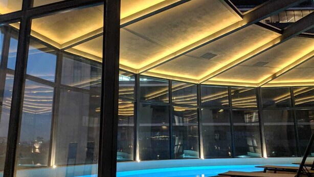 Una piscina interna moderna con pareti in vetro, un pavimento in legno e un design del soffitto geometrico.