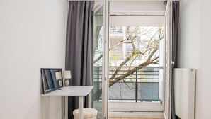 A bedroom with a bed, a desk, a chair, a radiator, and a sliding glass door to a balcony. - Rondo Wiatraczna Harmony Apartment (Warszawa)