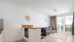 A modern apartment with a kitchen island, a grey sofa, and a large sliding glass door to the outside. - Rondo Wiatraczna Harmony Apartment (Warszawa)