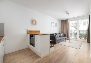 A modern apartment with a kitchen island, a grey sofa, and a large sliding glass door to the outside. - Rondo Wiatraczna Harmony Apartment (Warszawa)