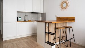 A modern kitchen with white cabinets, a wooden countertop, and two stools. - Rondo Wiatraczna Harmony Apartment (Warszawa)