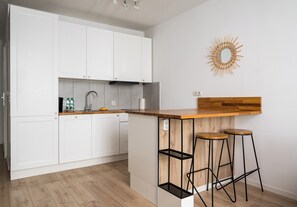A modern kitchen with white cabinets, a wooden countertop, and two stools. - Rondo Wiatraczna Harmony Apartment (Warszawa)