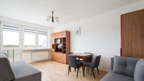A modern living room with a grey sofa, a wooden dining table with chairs, and a built-in TV unit. - Las Bielański Homely Apartment (Warszawa)