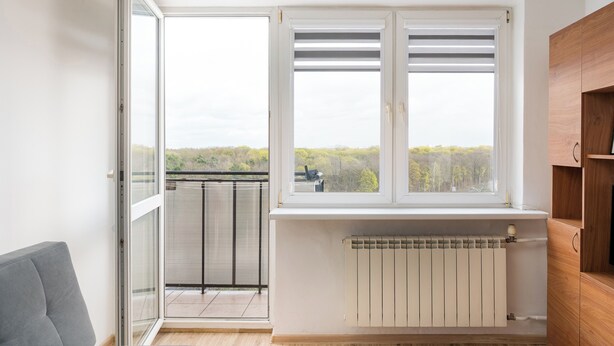 A room with a large window, a radiator, and a wooden cabinet. - Las Bielański Homely Apartment (Warszawa)