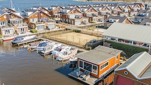Een jachthaven met aangemeerde boten, een groot houten gebouw met terras, en een woongebied met huizen.