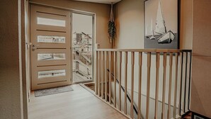 Een gang met een houten leuning, een deur met ruitpanelen en een ingelijst schilderij aan de muur.