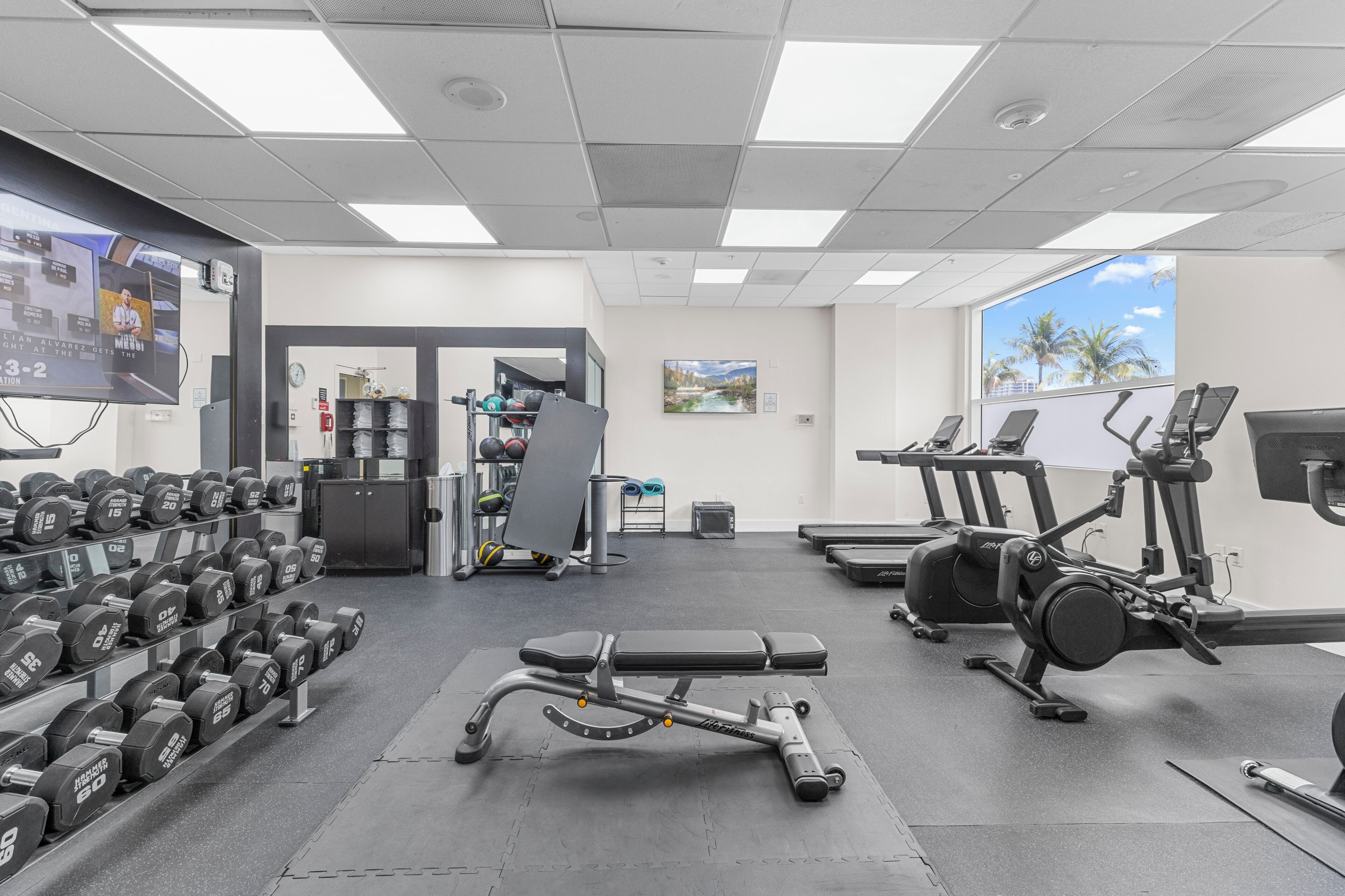 Un gimnasio con mancuernas, banco, cintas de correr y equipo de ejercicio.