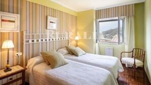 Una camera d'albergo con due letti, una finestra vista, un termosifone e una sedia.